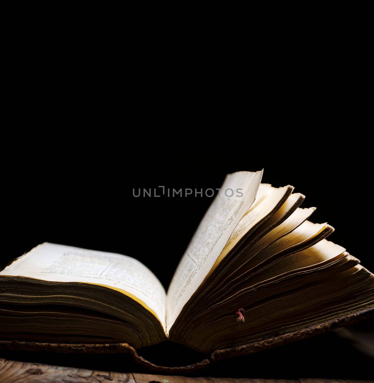 Old book open on vintage table on dark background. Read and study vintage bible with illuminated page. Literature and education still life.