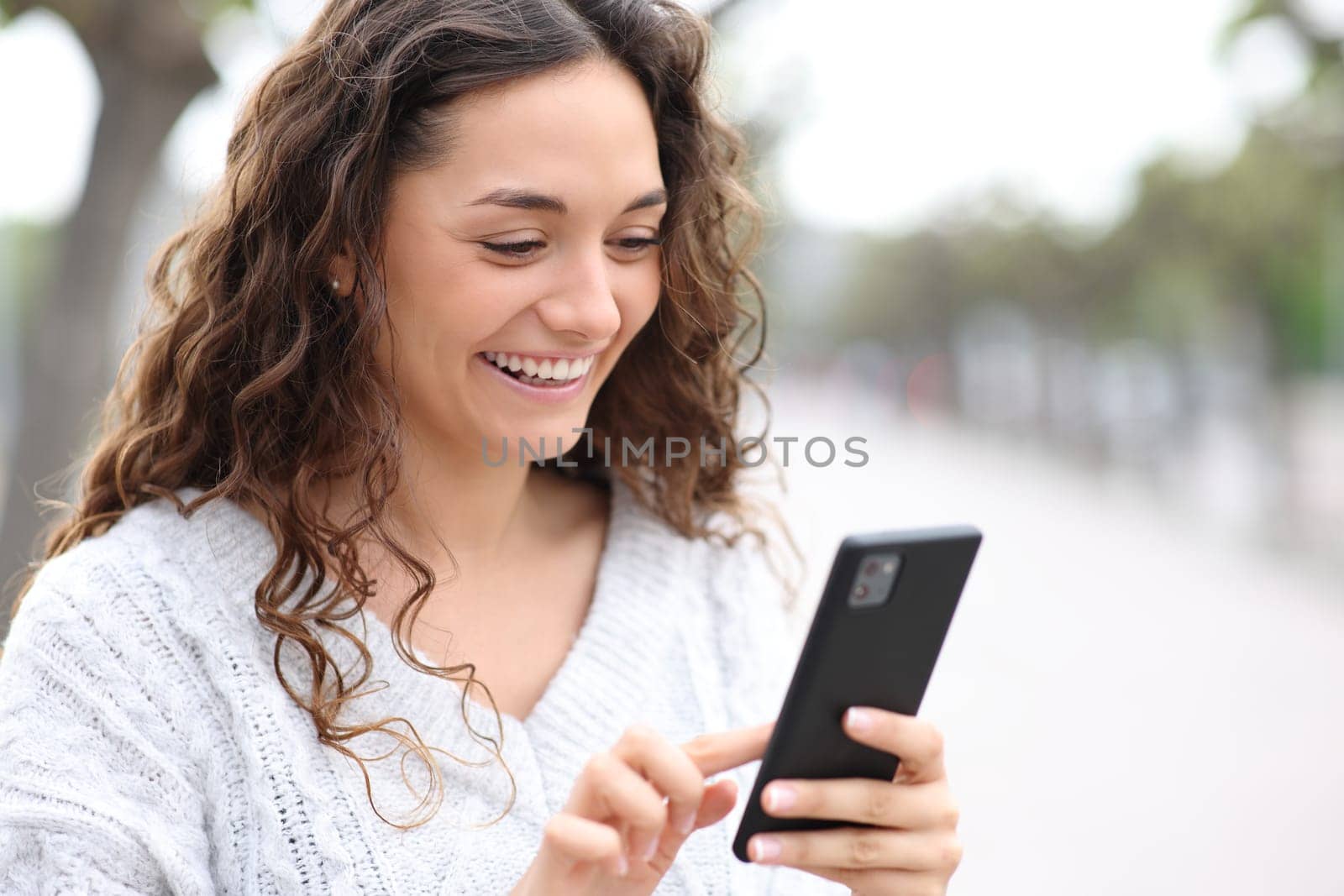 Happy woman using cell phone outside in the street