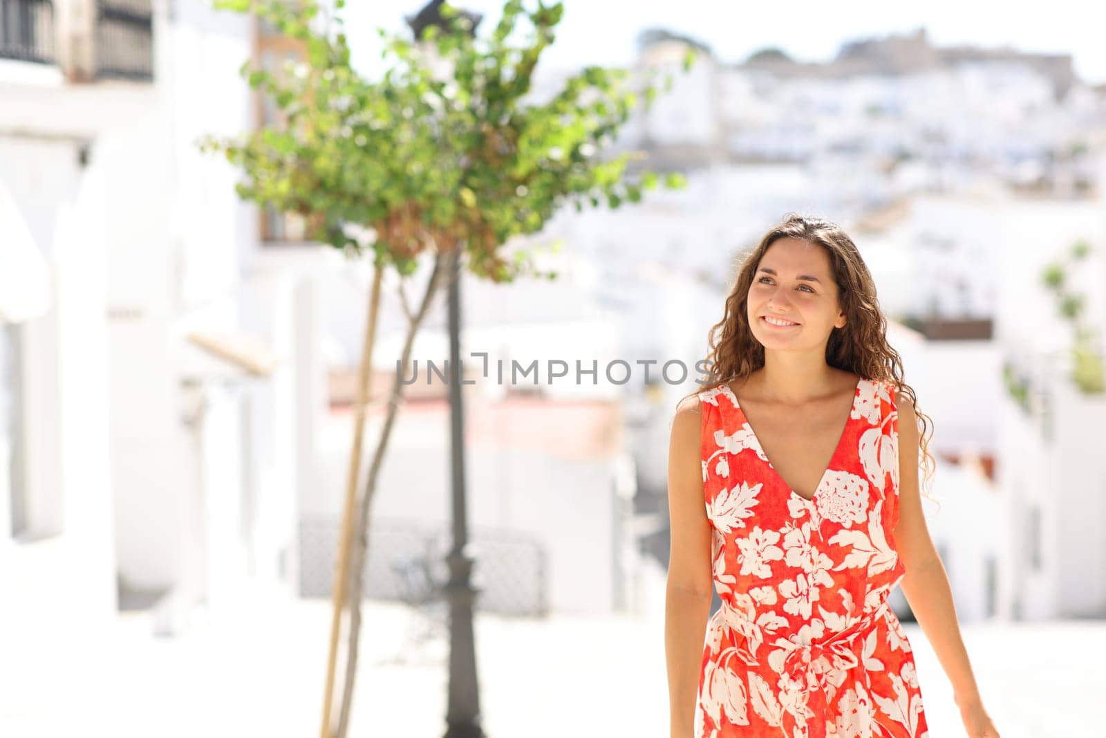 Front view portrait of a happy tourist walking and sightseeing in a white town