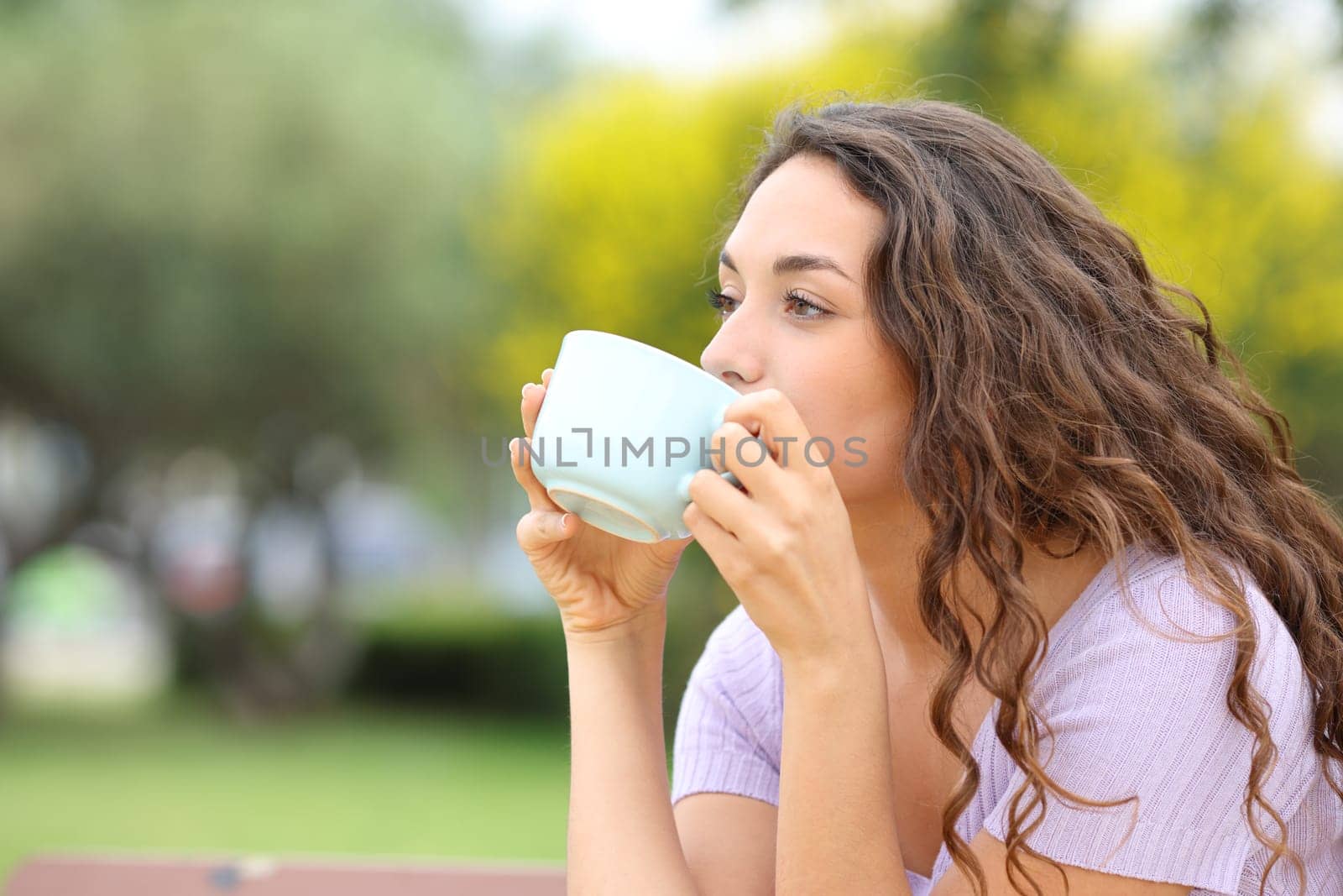 Woman drinking coffee sitting on a bench in a park