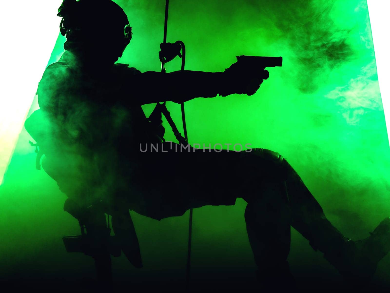 Silhouette of police officer in tactical gear descending from a height, rope exercises with weapons. Tactical rappelling, anti-terror or counter terrorism operation in darkness in rappelling harness