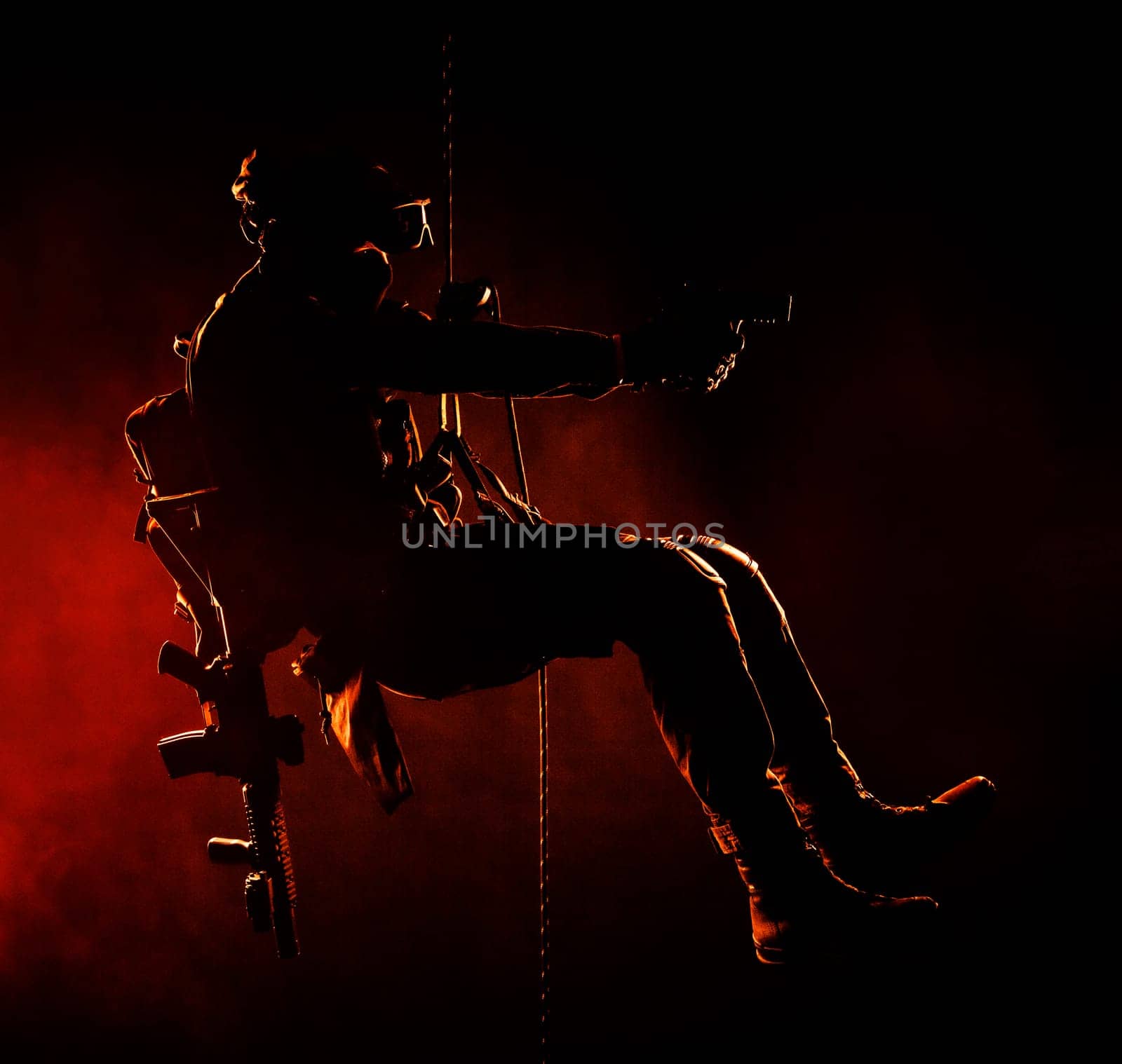 Silhouette of police officer in tactical gear descending from a height, rope exercises with weapons. Tactical rappelling, anti-terror or counter terrorism operation in darkness in rappelling harness