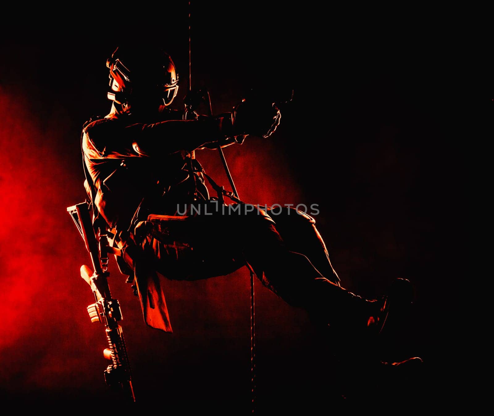 Silhouette of police officer in tactical gear descending from a height, rope exercises with weapons. Tactical rappelling, anti-terror or counter terrorism operation in darkness in rappelling harness
