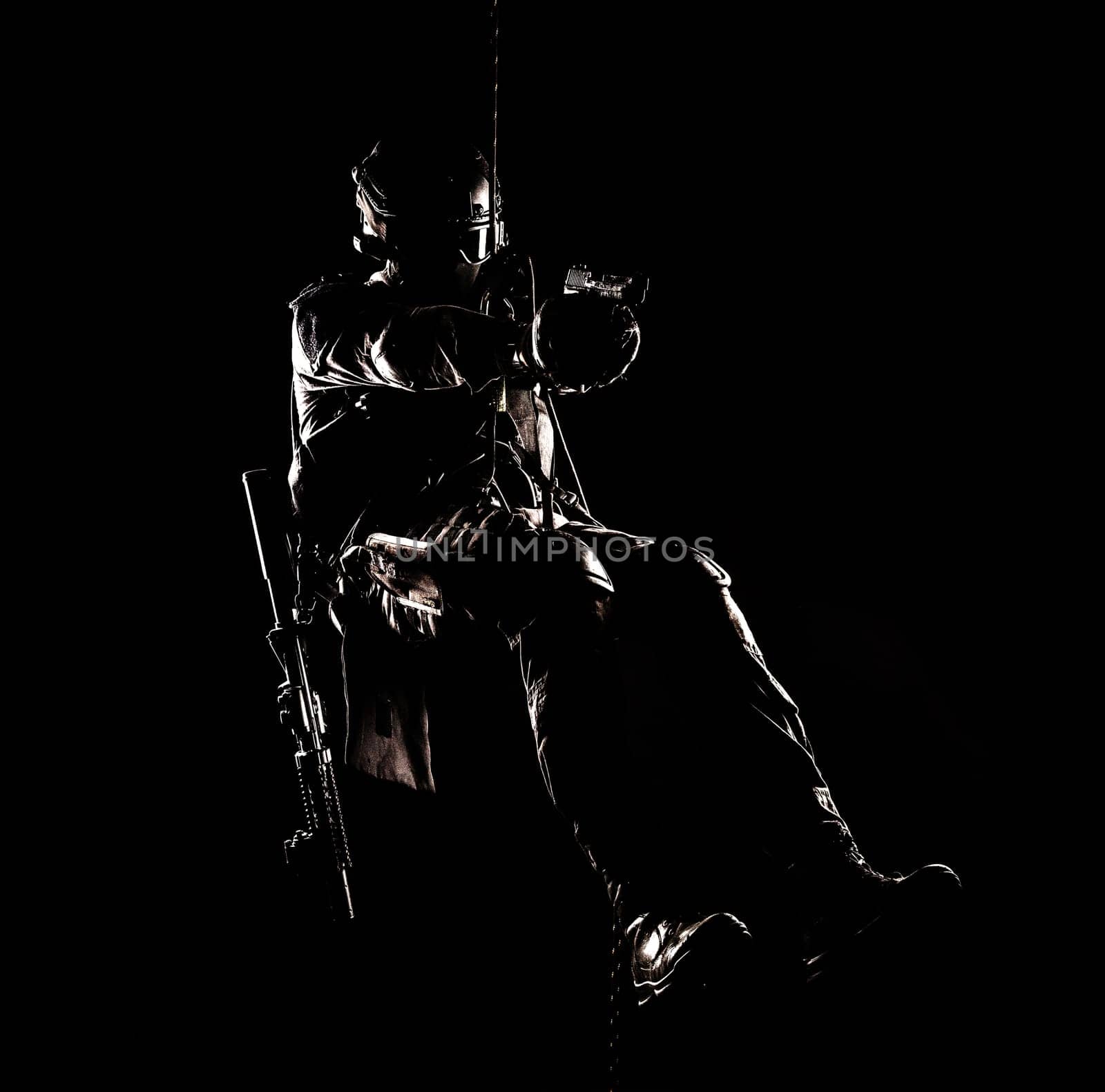 Silhouette of police officer in tactical gear descending from a height, rope exercises with weapons. Tactical rappelling, anti-terror or counter terrorism operation in darkness in rappelling harness
