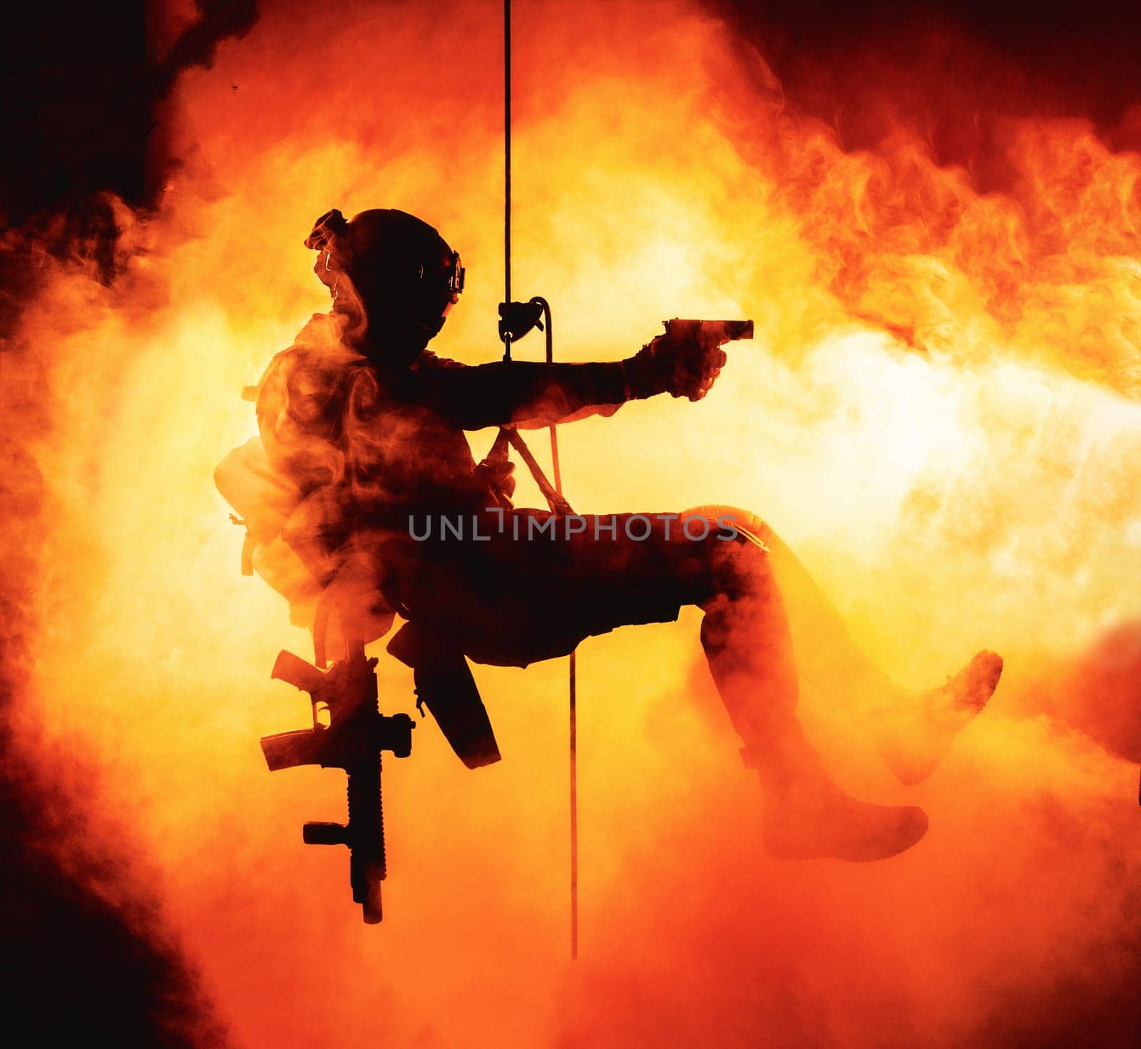Silhouette of police officer in tactical gear descending from a height, rope exercises with weapons. Tactical rappelling, anti-terror or counter terrorism operation in darkness in rappelling harness