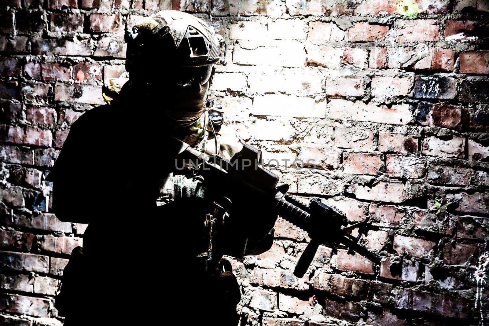A silhouette of soldier in action in a ruined building, sneaking in darkness along brick wall. Concept of urban military war conflict