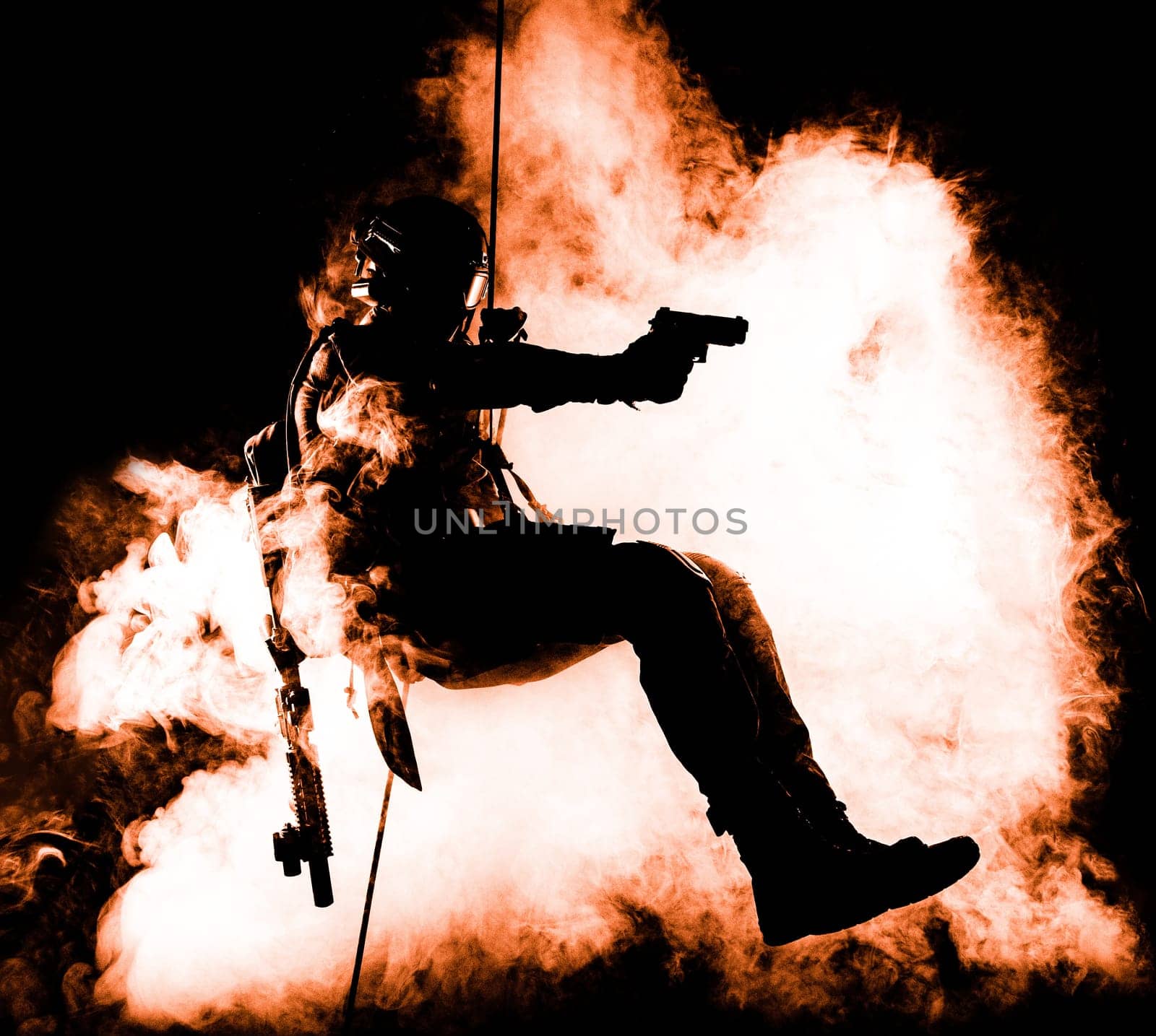 Silhouette of police officer in tactical gear descending from a height, rope exercises with weapons. Tactical rappelling, anti-terror or counter terrorism operation in darkness in rappelling harness