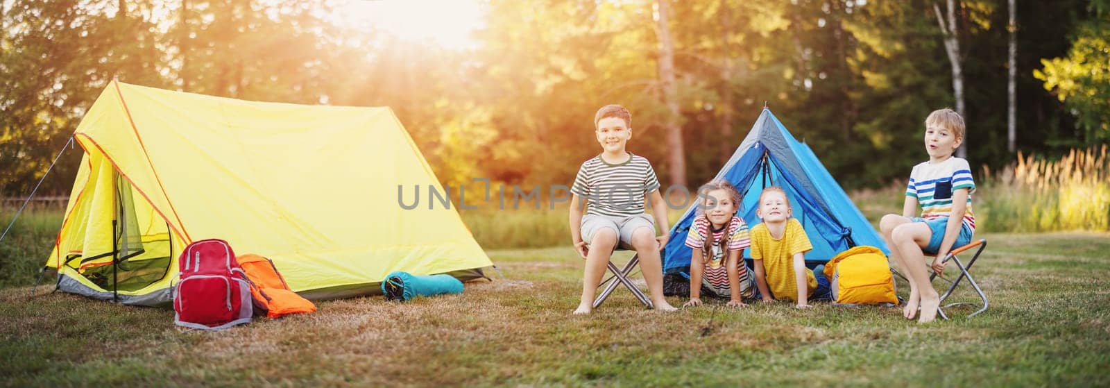 Group of children resting in the campground in nature. Concept of the family vacation, recreation and scouts camping.