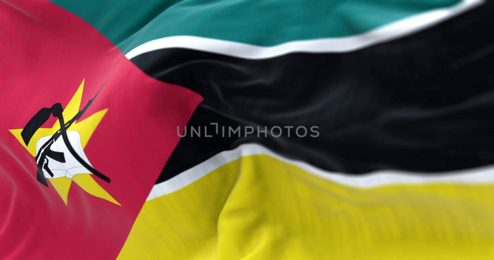 Detail of the Mozambique flag waving. green, black, and yellow stripes, red triangle, yellow star, crossed book, hoe, and AK-47. 3d illustration render. Selective focus. Close-up. Textured background