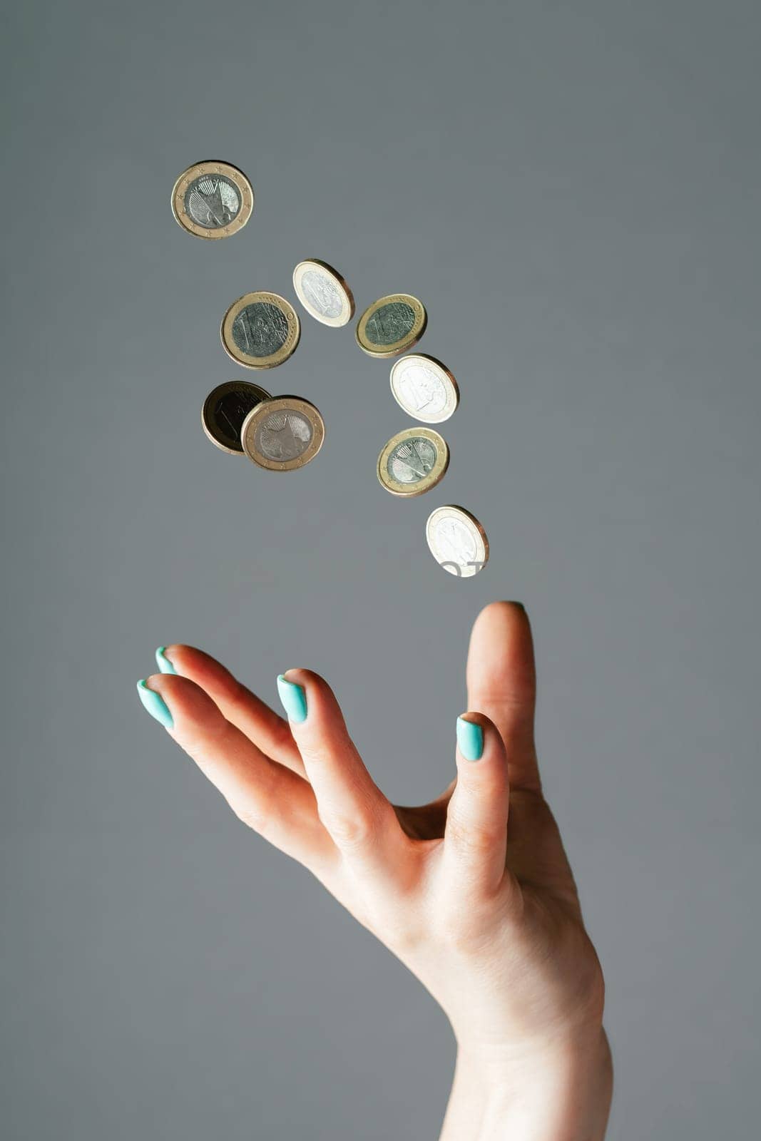 Female hand with blue nails throwing money, one euro coins into air on gray background. Levitating cash. Copy space, vertical