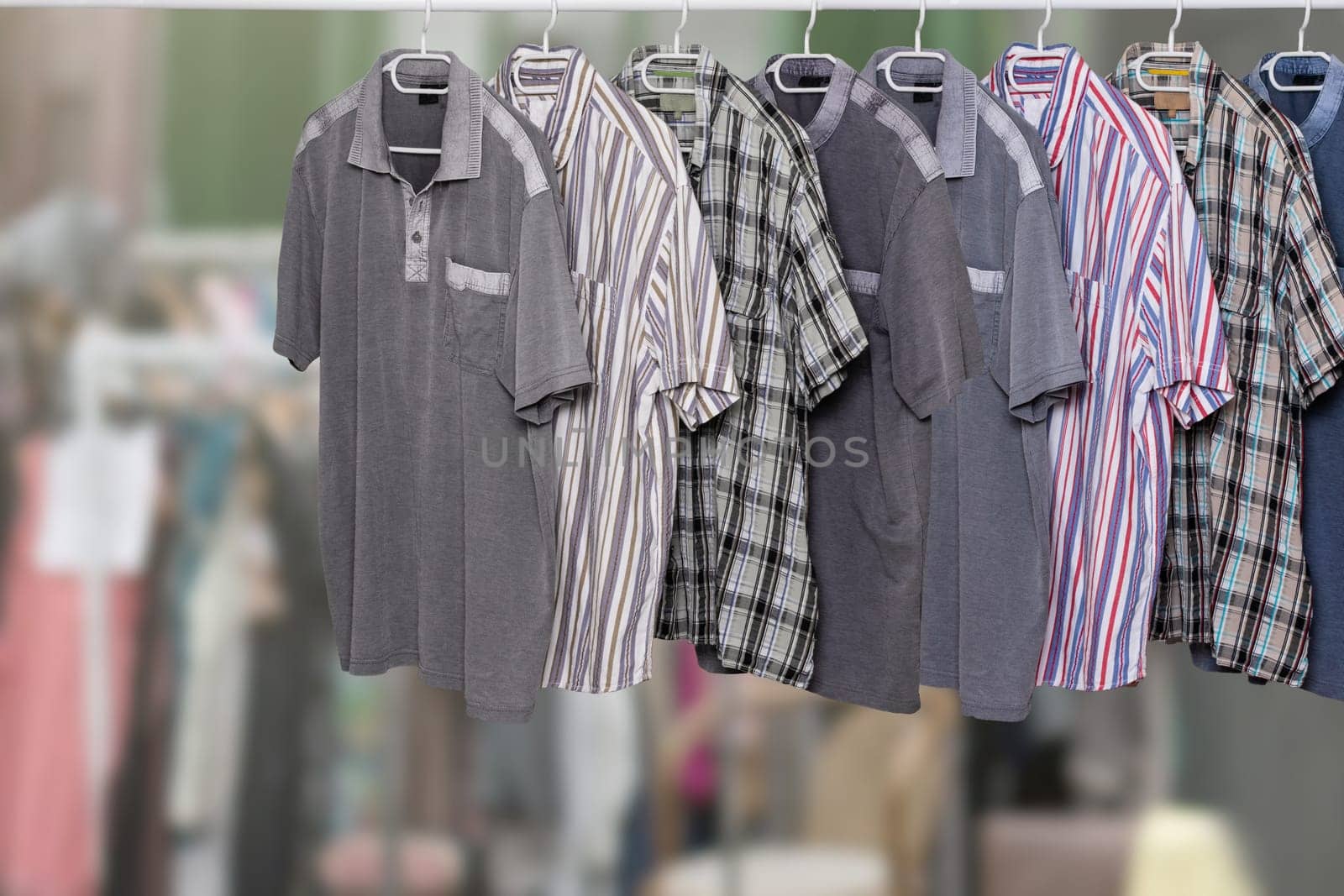 Clothes on rack. Clothing rack with various colorful male casual summer shirts over abstract blurred clothes shop. All hanging neatly on hangers at cloth rail. Space. Shopping.