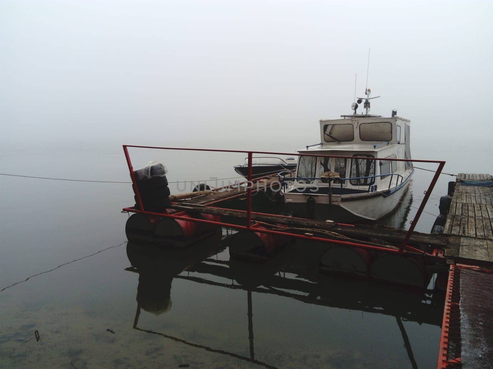 Belgrade, Serbia, January 14, 2020 White boat at the pier, left for the winter. Foggy weather on a January cloudy day. Reflection in the river river. House for shelter from the weather.