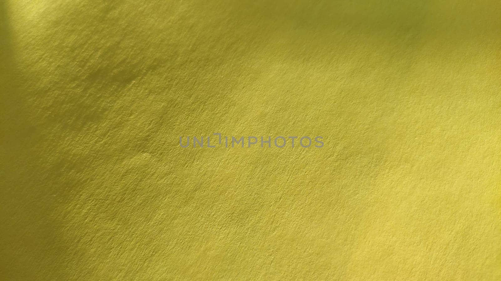 The paper or fabric material is bright yellow. Close-up. Slightly folded sheet. Light gradient and accentuated rough surface texture. Background or product sample. Sunny cheerful yellow.