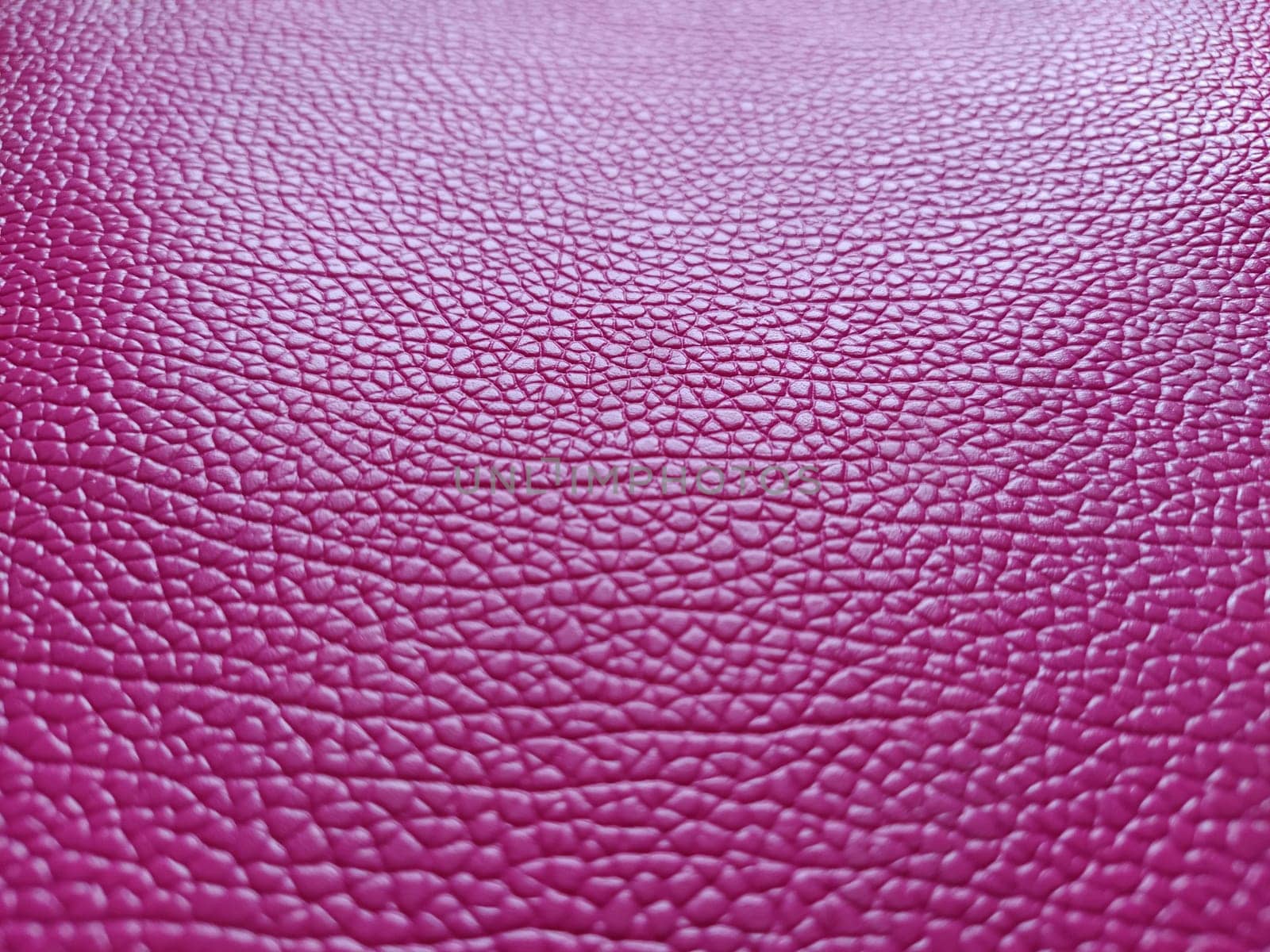 Artificial leather is bright pink or fuchsia. Distinct furrows and elevations on the surface of a bag or shoe. Reflection of the light. Fashion accessory made of imitation pig skin. Close-up.