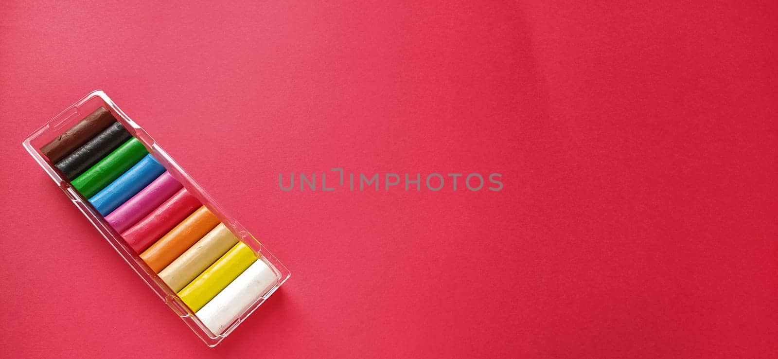 Multi-colored new plasticine in plastic packaging on a red background. Plasticine plates of red, pink, green, white, yellow, brown, blue, black. Set for children's creativity.