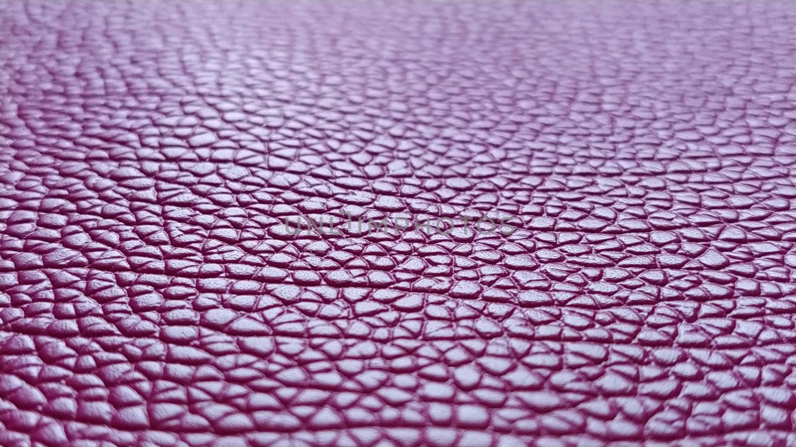 Artificial leather is bright pink or fuchsia. Distinct furrows and elevations on the surface of a bag or shoe. Reflection of the light. Fashion accessory made of imitation pig skin. Close-up.