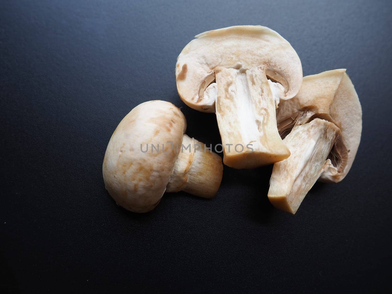 Champignons on a black background. Sliced and whole fresh uncooked raw mushrooms. Cooking mushrooms with a recipe