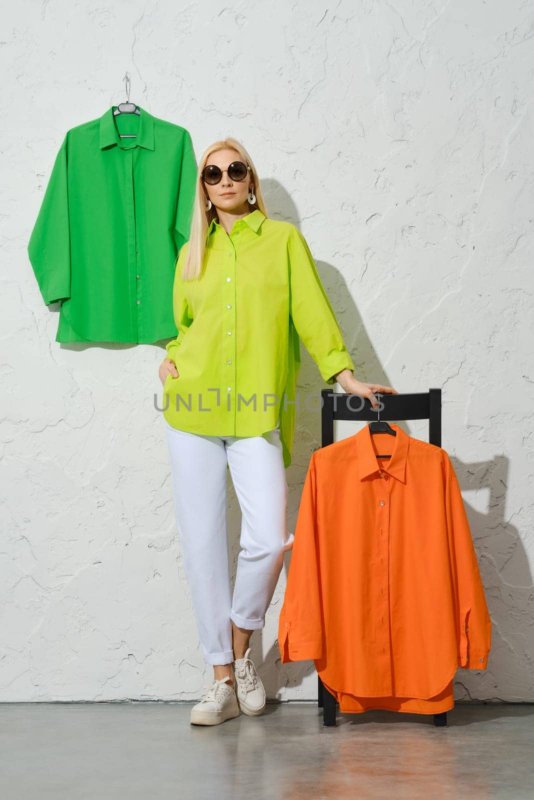 Trendy woman in sunglasses, light green shirt and white jeans leaning against tall stool