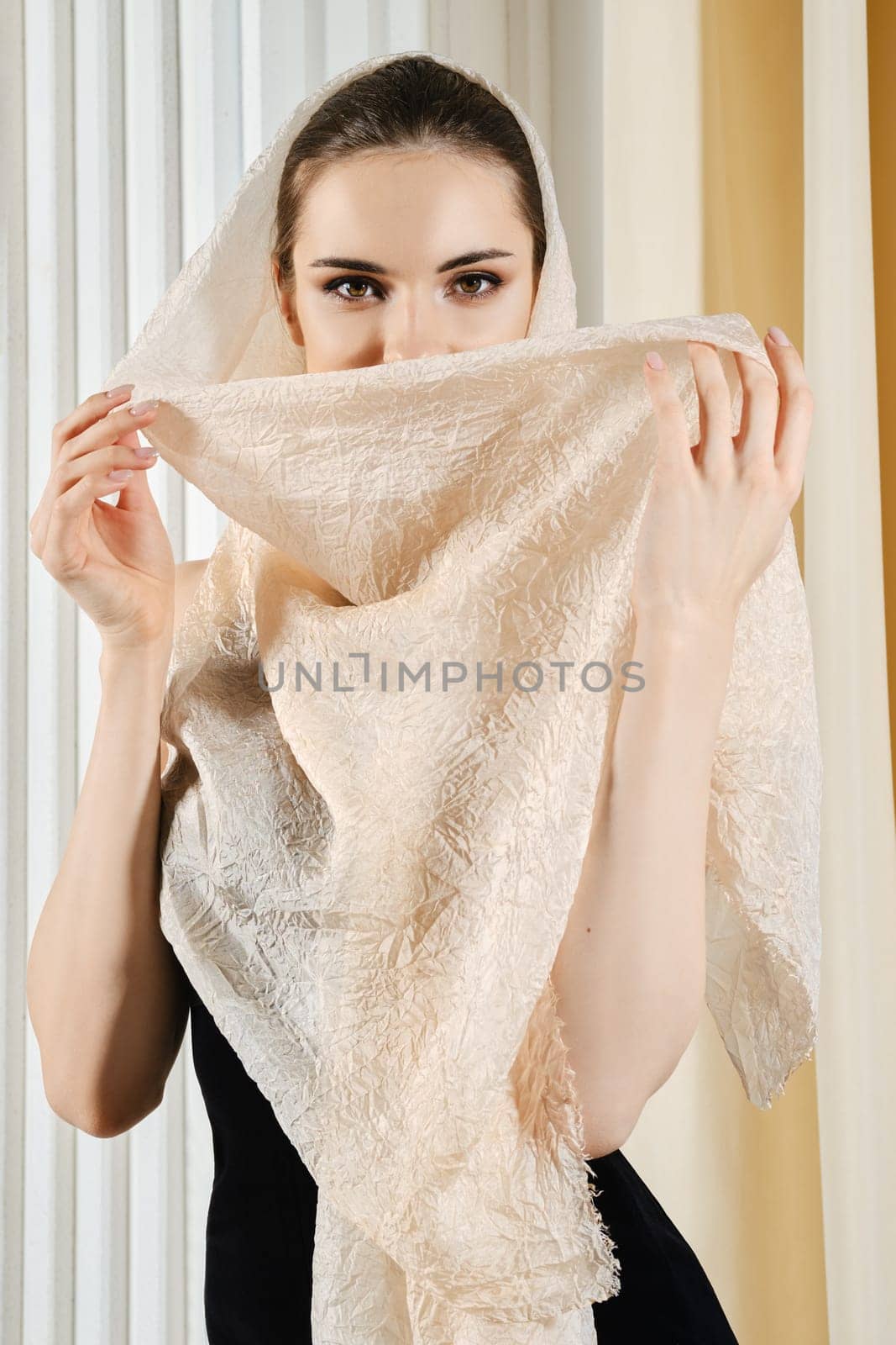 Elegant young woman covers her face with silk headscarf