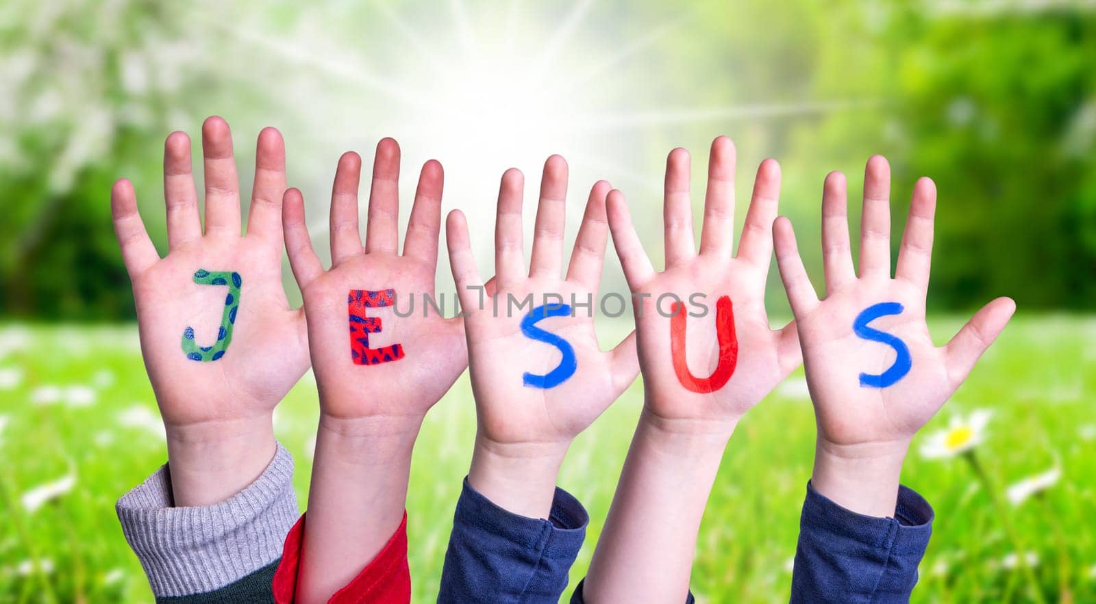 Children Hands Building Colorful English Word Jesus. Sunny Green Grass Meadow As Background.