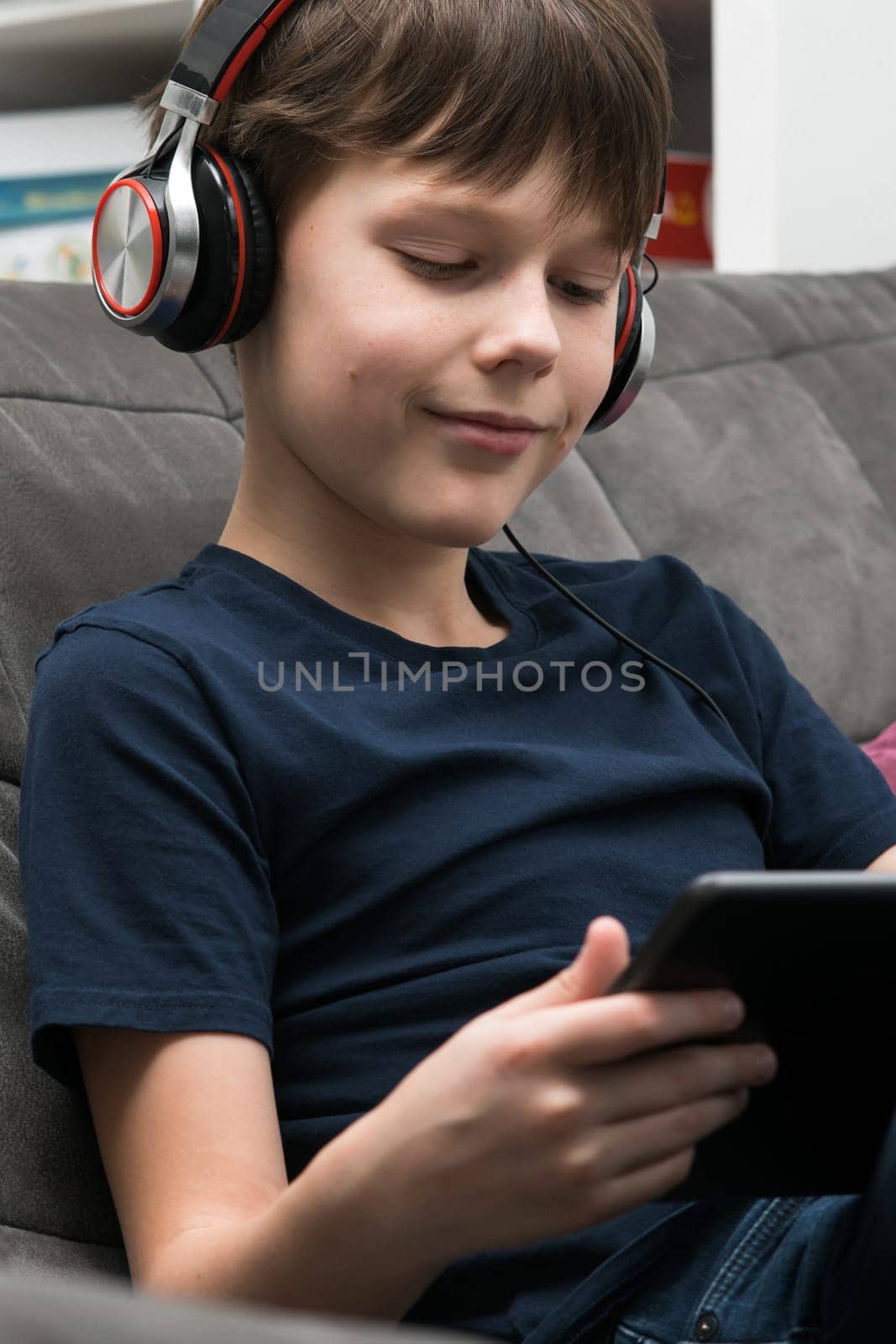 Portrait of happy little boy with digital tablet computer. Child in headphones play videogame on gadget or listen to music. Tablet in hands, home leisure, gamer, modern electronics.