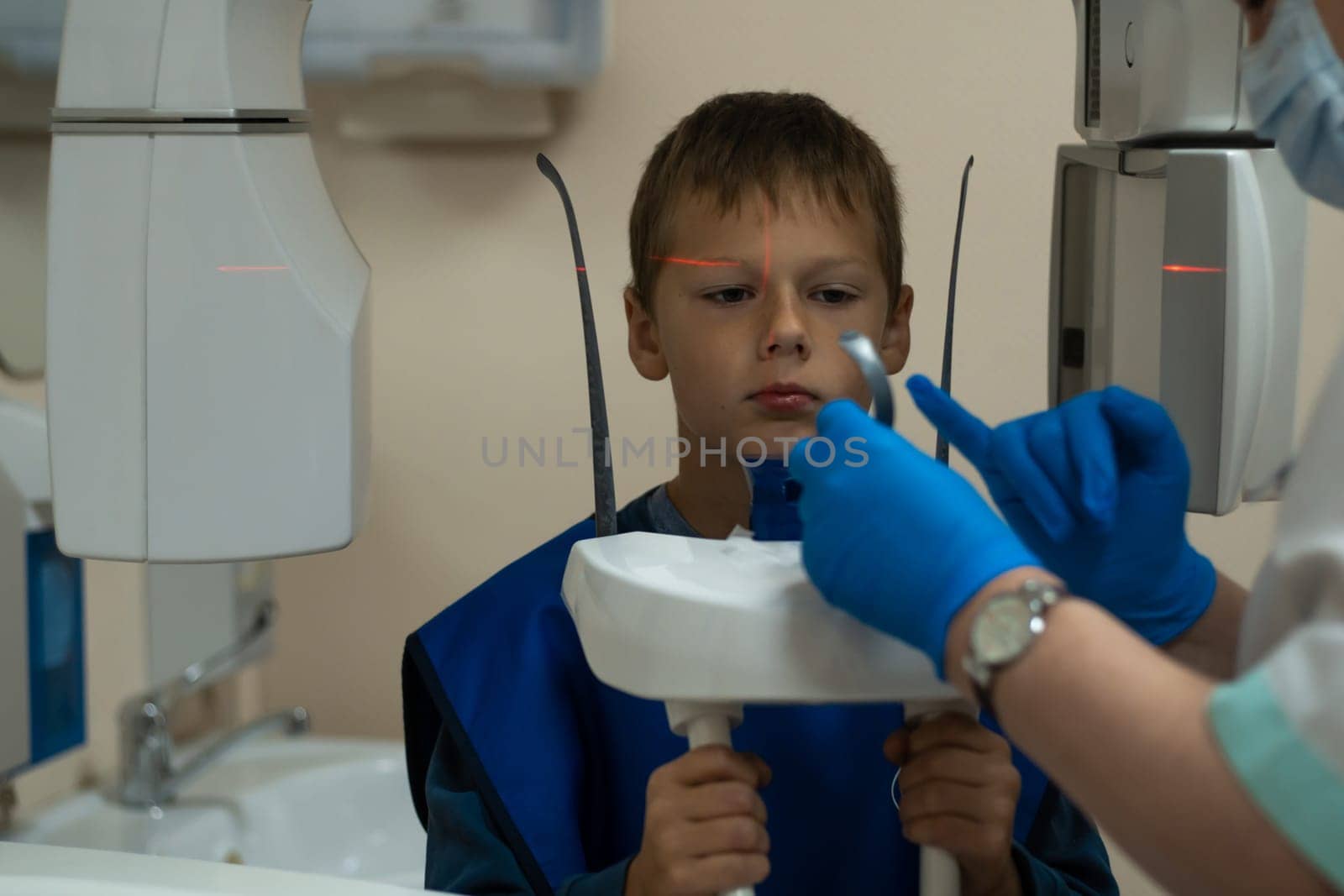 Jaw computed tomography, check up teeth in dental clinic. Boy in vest on x-ray diagnostics. Hands of radiologist in medical gloves do circular snapshot of jaw on modern medical equipment. CT scanning.