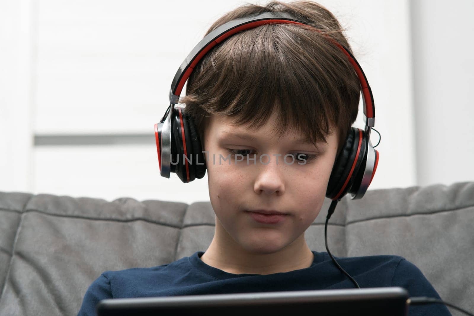 Portrait of little boy with digital tablet computer. Child in wired headphones play videogame on gadget or listen to music. Online entertainment, home leisure, gamer, modern electronics.