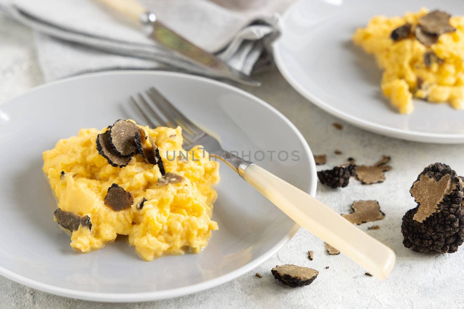 Scrambled eggs with sliced fresh black truffles from Italy served in a plate near fork and knife close up. Italian cousine, gourmet breakfast