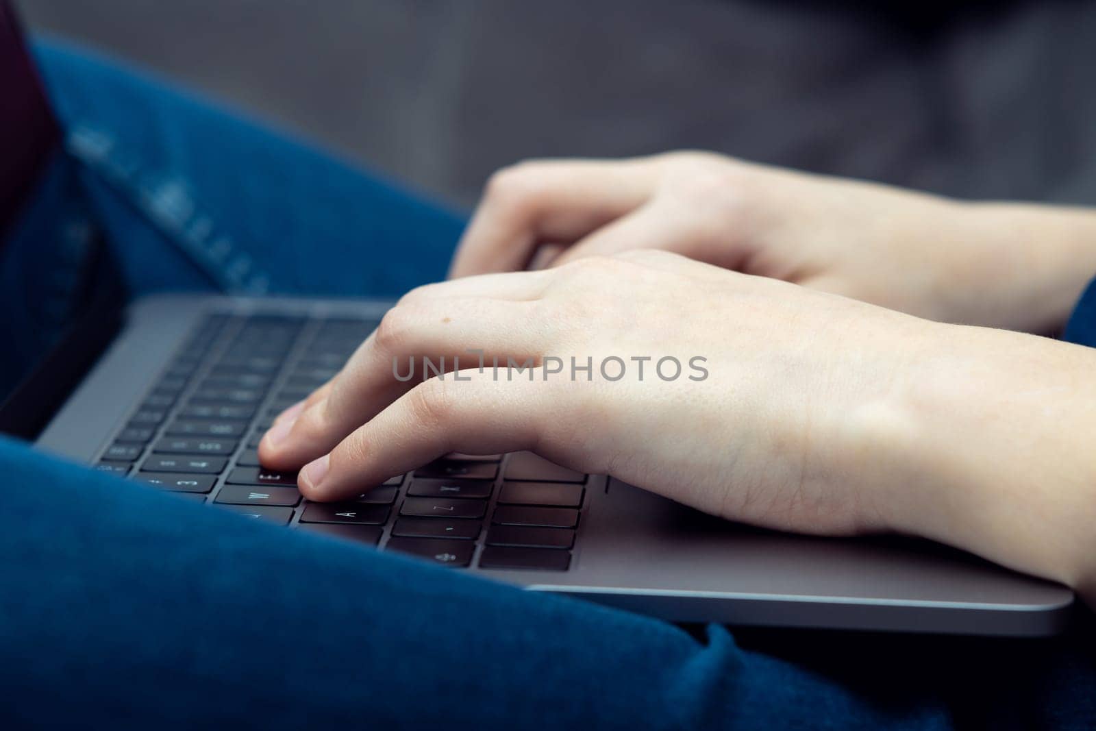 Digital laptop computer on male legs, side view closeup. Young business man typing on keyboard of portable modern notebook. Working on multitasking gadget. High technology, IT sphere, electronics.