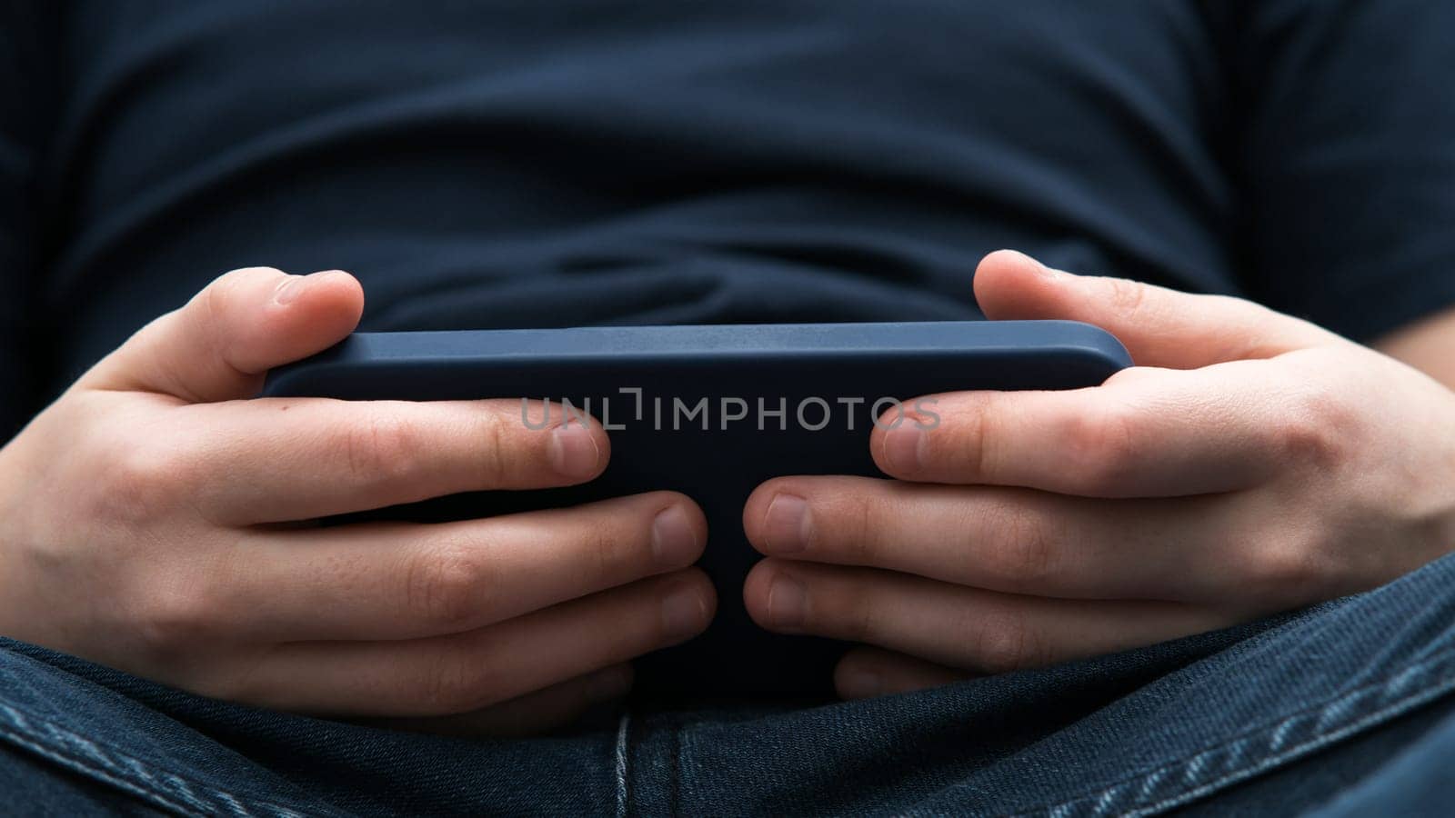 Male hands play videogames on smartphone closeup. Young guy using mobile phone to play game or watch online video content. Entertainment, modern gadget, touchscreen, digital electronics.