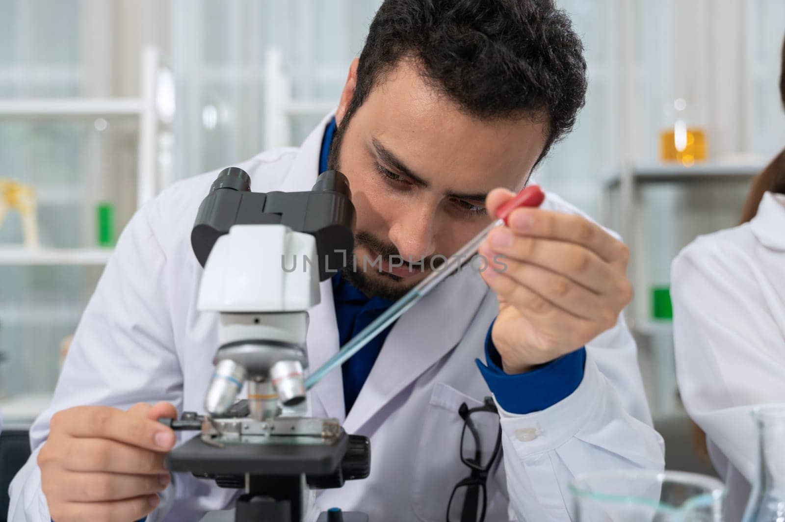 Male scientist in white lab coat dropping chemical liquid on slide and using microscope in laboratory research and development. Science and Technology concept
