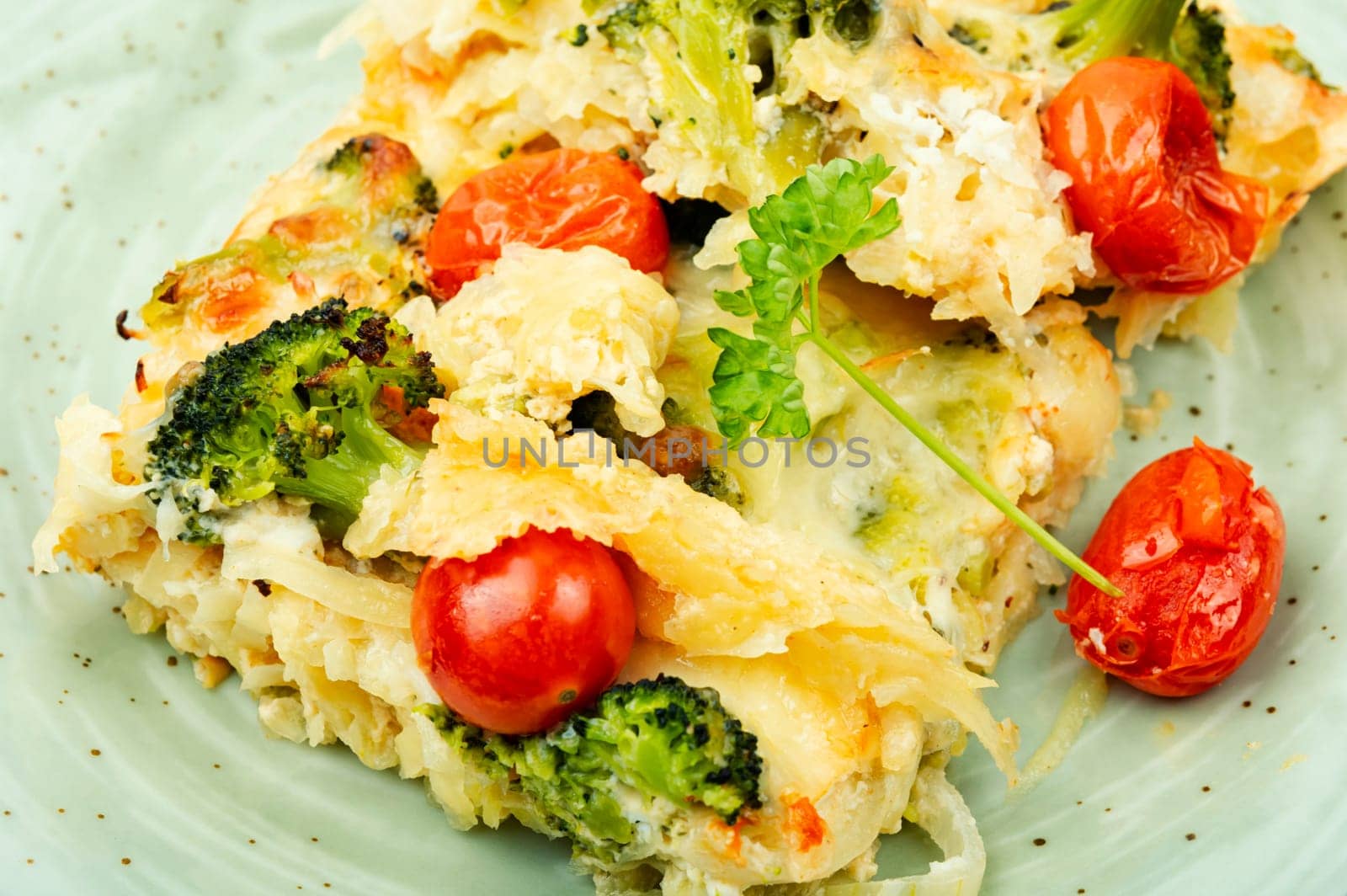 Appetizing potato casserole with broccoli and tomatoes on a plate.