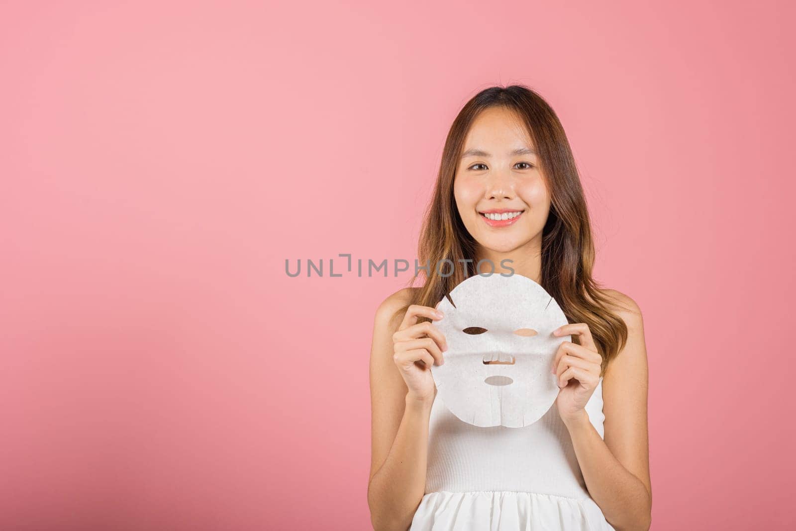 Healthcare spa. Asian woman holding purifying mask face on hands, Portrait beautiful female smiling holds facial sheet mask, Studio shot isolated on blue background, Face care and beauty treatments