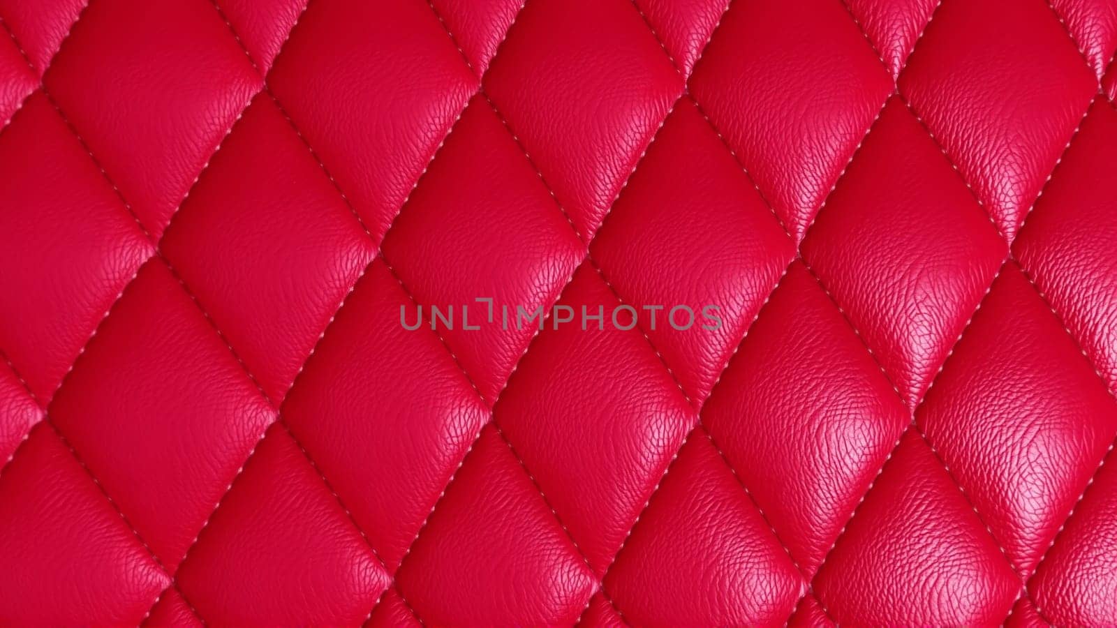 The surface texture of artificial leather in red, stitched in the form of rhombuses, squares, rectangles. Quilted eco-leather. High quality photo