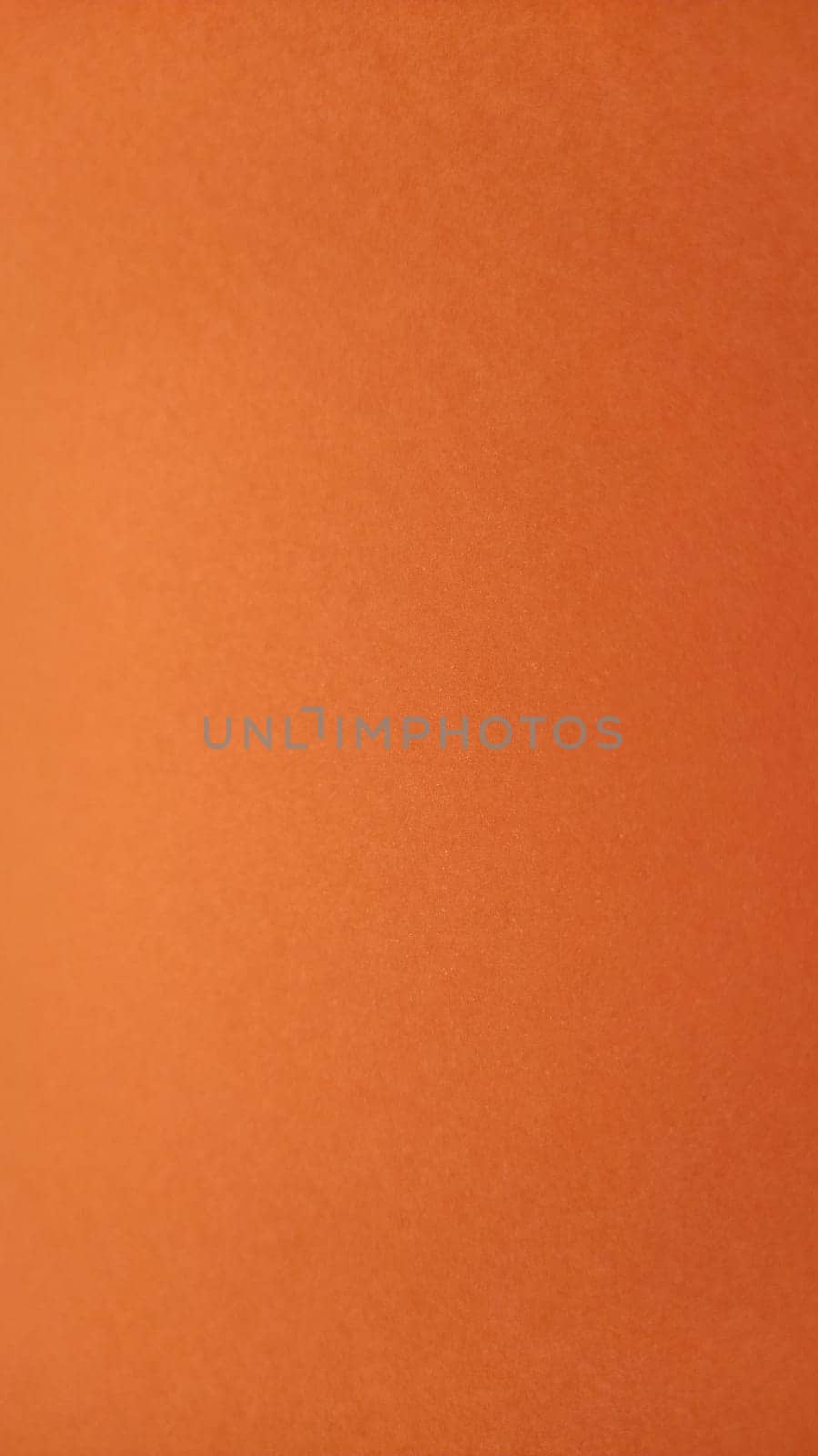 A sheet of thick paper of bright orange color. Close-up. Background intense shade. Natural lateral lighting. Fine cardboard or paper texture. Light gradient in degree of illumination. Copy space.