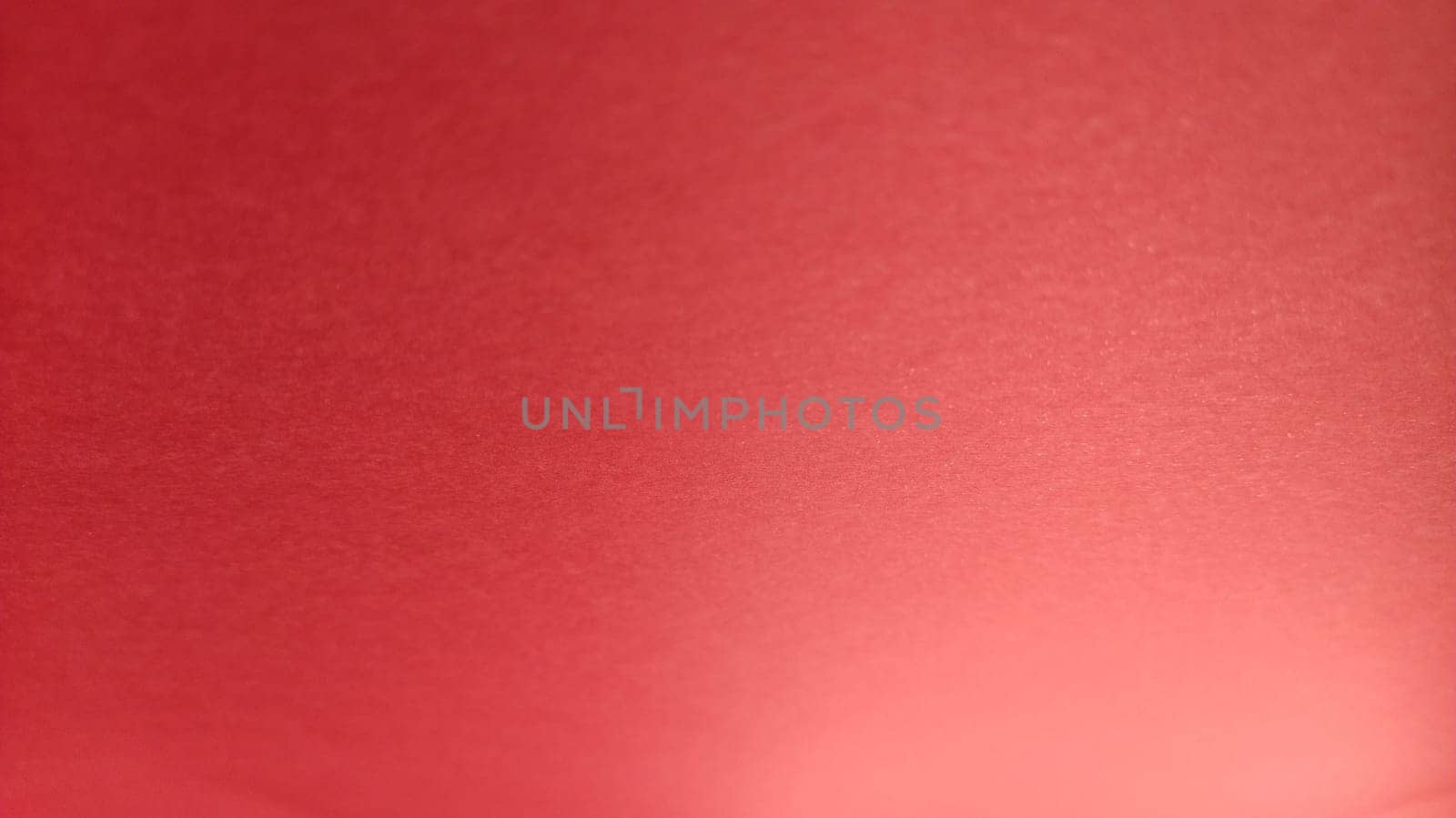 Beautiful red bright background. Color gradient depending on the lighting. Scarlet uneven color. A sheet of colored paper with natural light. Fragment of a sheet of colored paper with a glare of light