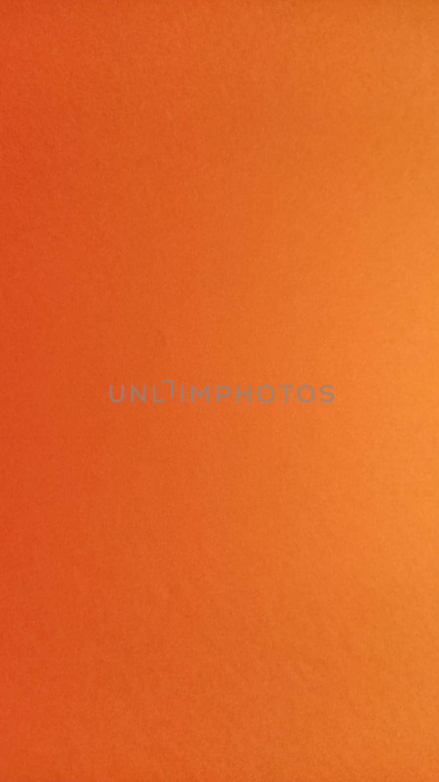 A sheet of thick paper of bright orange color. Close-up. Background intense shade. Natural lateral lighting. Fine cardboard or paper texture. Light gradient in degree of illumination. Vertical image