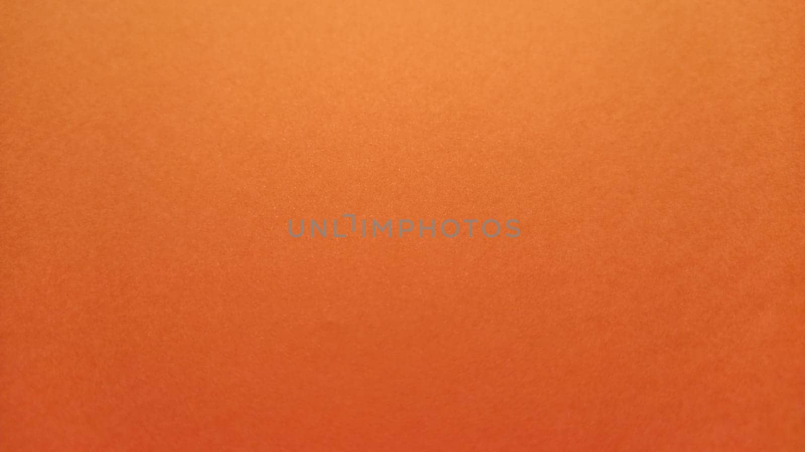 A sheet of thick paper of bright orange color. Close-up. Background intense shade. Natural lateral lighting. Fine cardboard or paper texture. Light gradient in degree of illumination. Copy space.