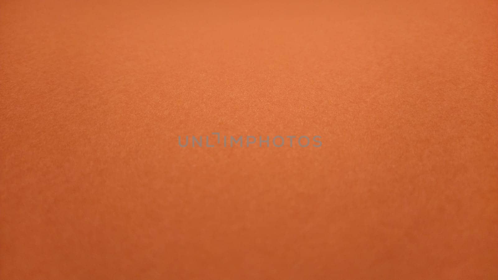 A sheet of thick paper of bright orange color. Close-up. Background intense shade. Natural lateral lighting. Fine cardboard or paper texture. Light gradient in degree of illumination. Copy space.