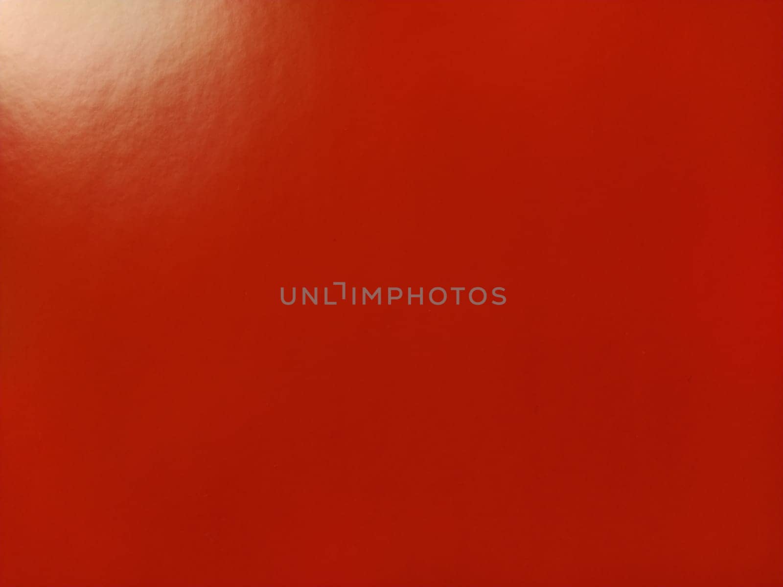 Beautiful bright red background. Closeup sheet of shiny reflecting incident light paper. Pure fun color. Intense shade of red, close to scarlet or blood color with high reflectivity