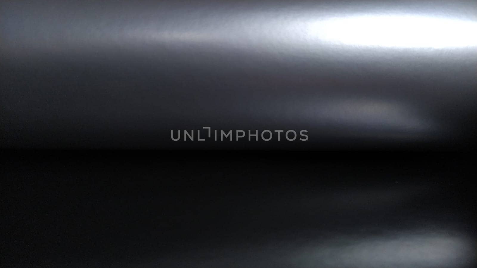 Gradient on a gray-black background. Horizontally folded shiny paper or foil with overflow and highlights. Mysterious radiance. Luxurious fabric. Metallic cold shine