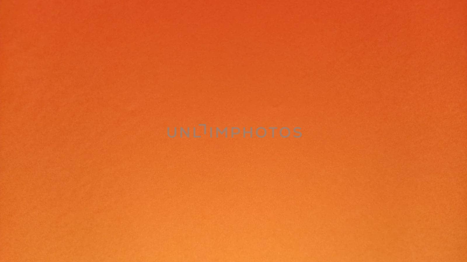 A sheet of thick paper of bright orange color. Close-up. Background intense shade. Natural lateral lighting. Fine cardboard or paper texture. Light gradient in degree of illumination. Copy space