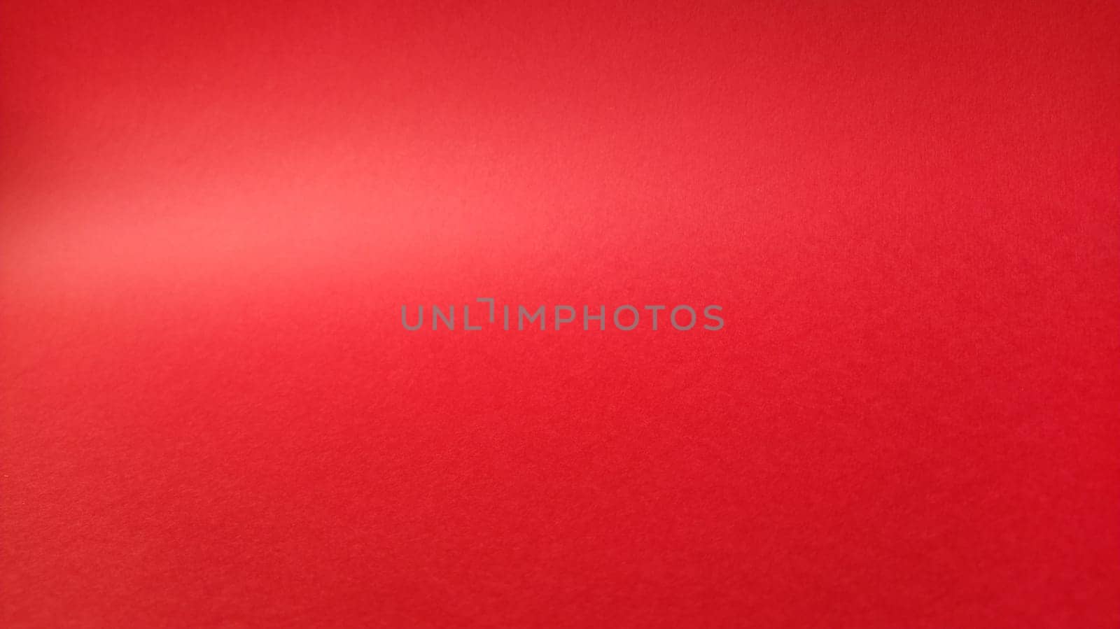 Beautiful red bright background. Color gradient depending on the lighting. Scarlet uneven color.A sheet of colored paper with natural light. Fragment of a sheet of colored paper with a glare of light.