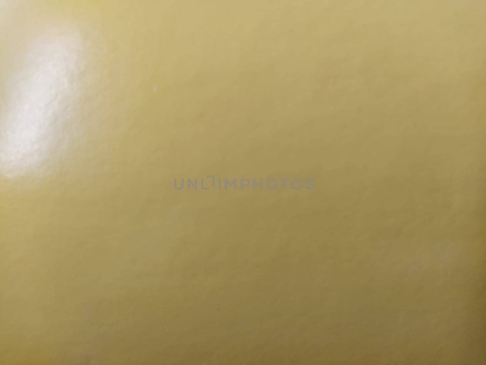 A beautiful pale yellow background close to beige. A sheet of shiny paper reflecting the incident light from the top left. A calm shade of yellow-beige. High reflectivity.