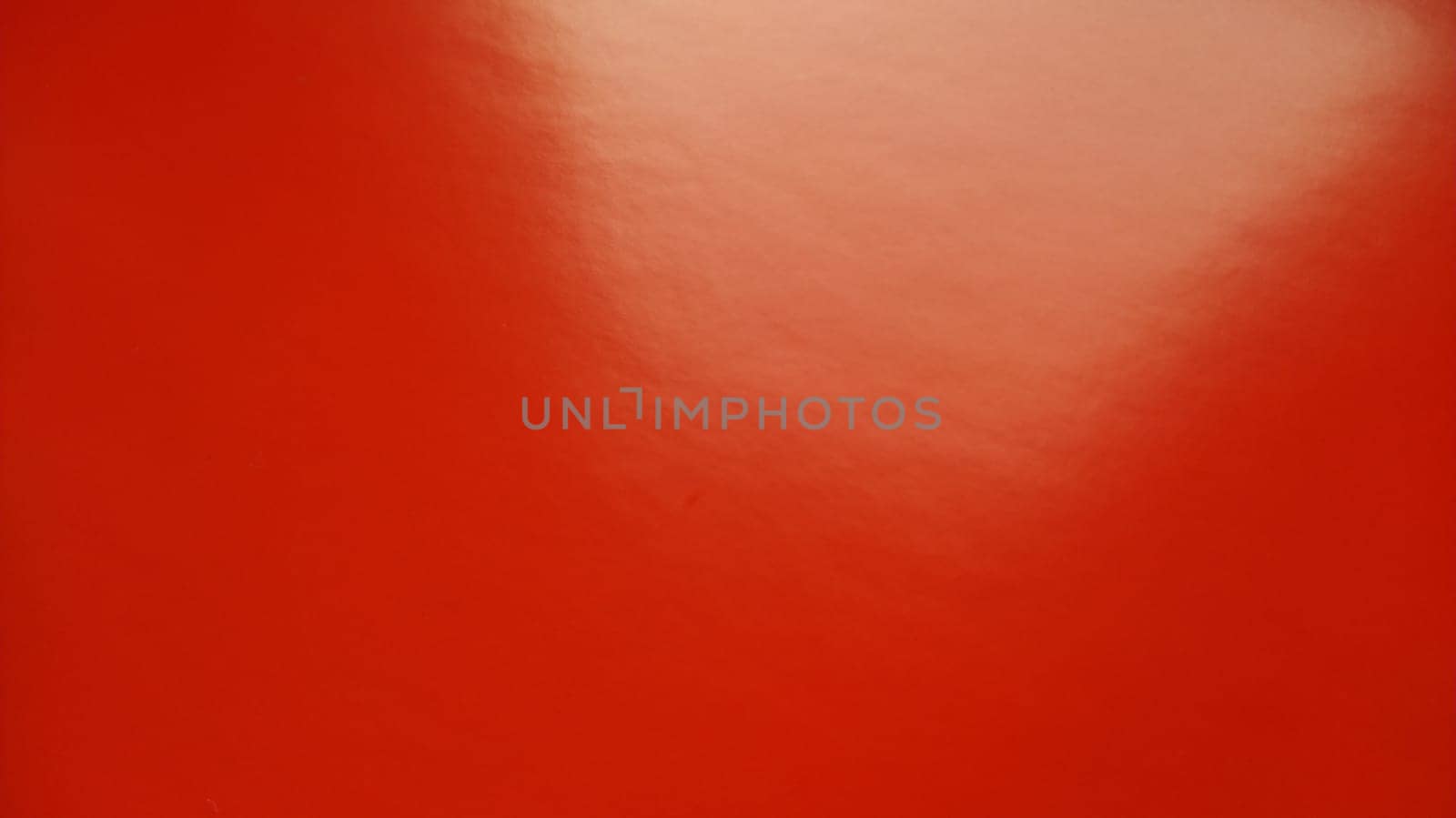 Beautiful bright red background. Closeup sheet of shiny reflecting incident light paper. Pure fun color. Intense shade of red, close to scarlet or blood color with high reflectivity