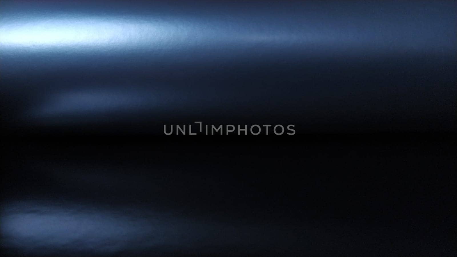 Gradient on a dark blue background. Horizontally folded shiny paper or foil with overflow and highlights. Mysterious radiance. Luxurious fabric. Metallic cold shine