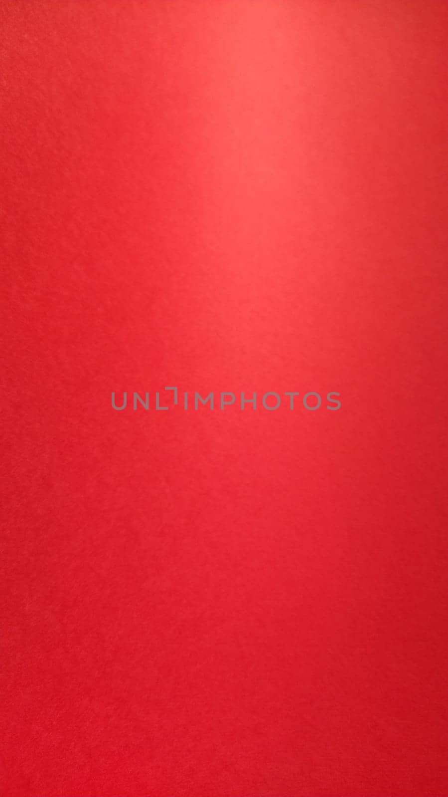 Beautiful red bright background. Color gradient depending on the lighting. Scarlet uneven color. A sheet of colored paper with natural light. Fragment of a sheet of colored paper with a glare of light