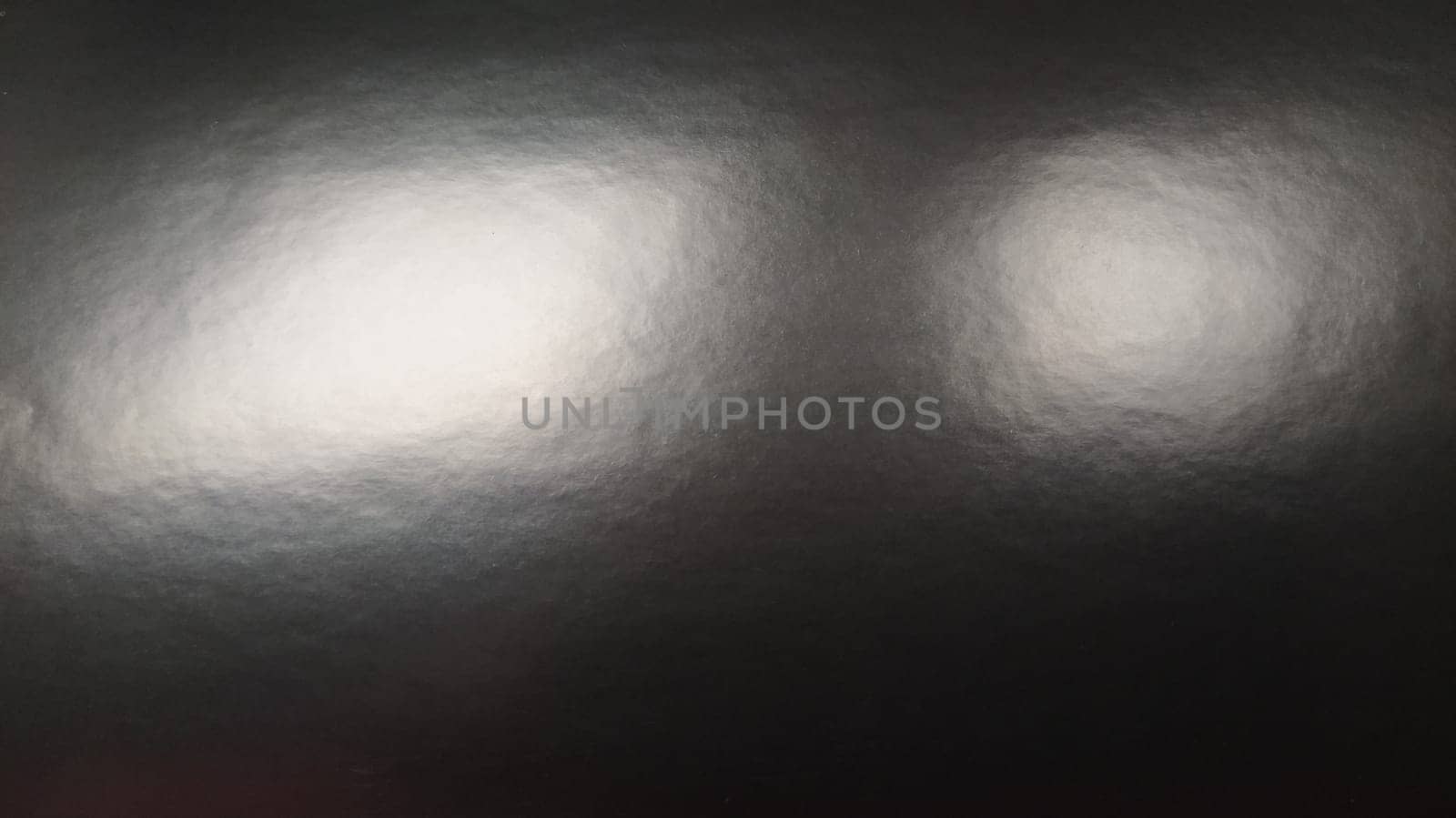 Glare of light on shiny gray paper. Several light spots on a dark surface that reflects light. Abstract monochrome background