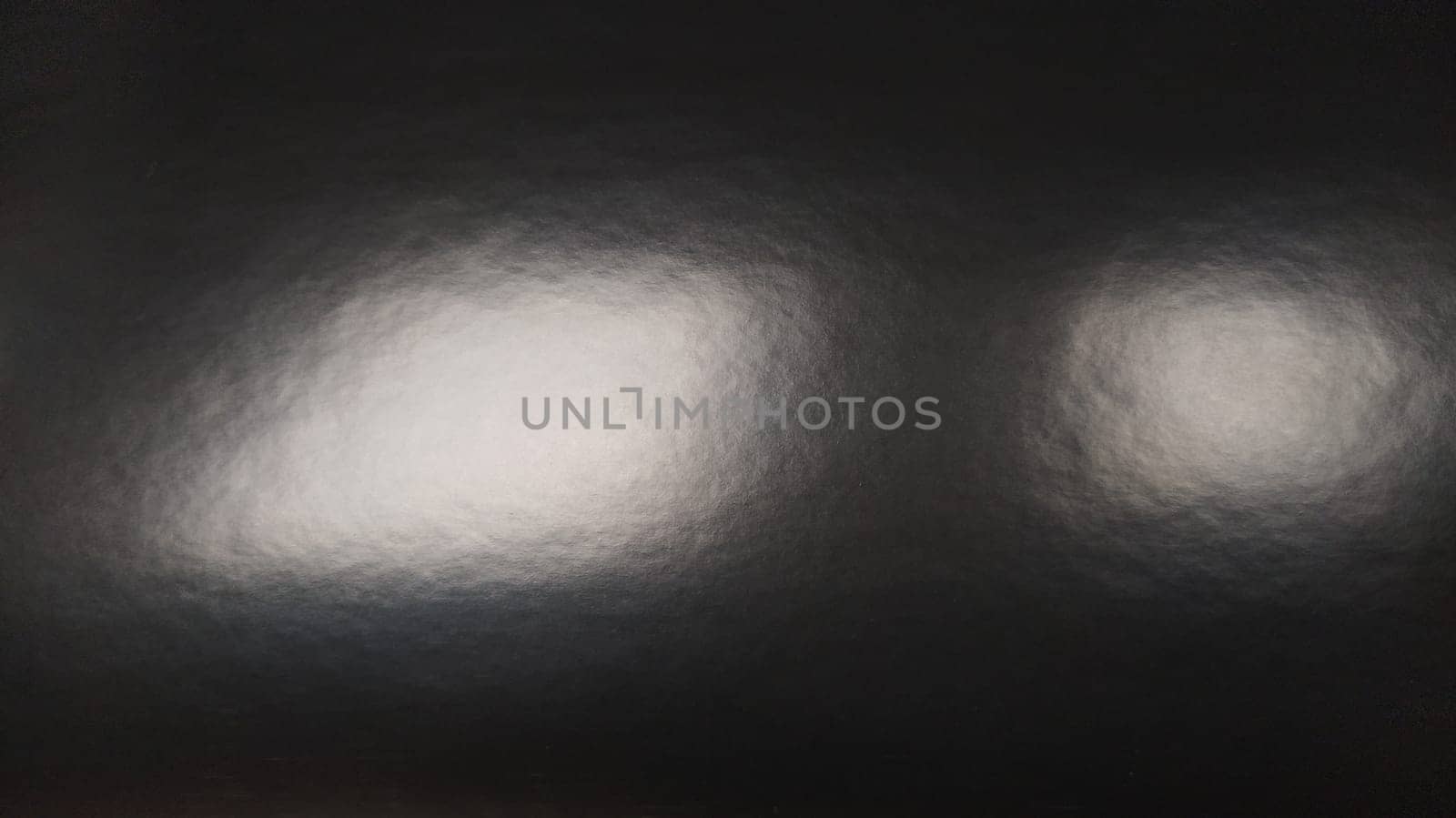Glare of light on shiny gray paper. Several light spots on a dark surface that reflects light. Abstract monochrome background
