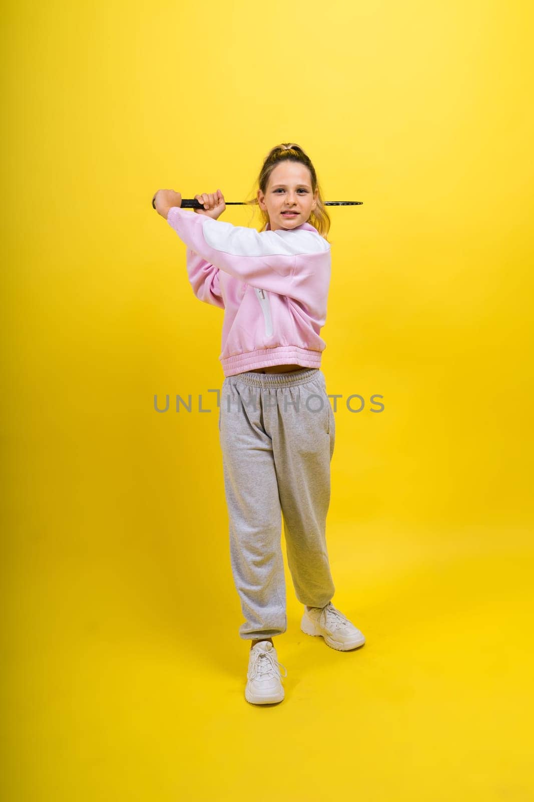 Full length studio photo of ten year old girl holding a badminton racket and isolated on yellow.